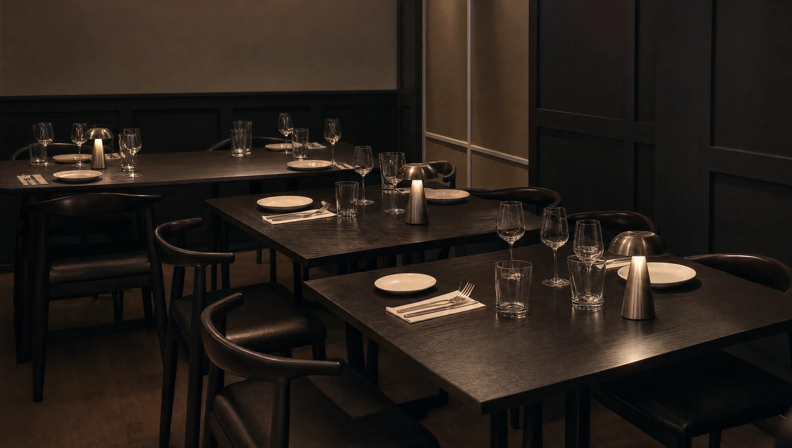 Ma lié dining room with black tables, curved black chairs, white plates and softly glowing table lamps