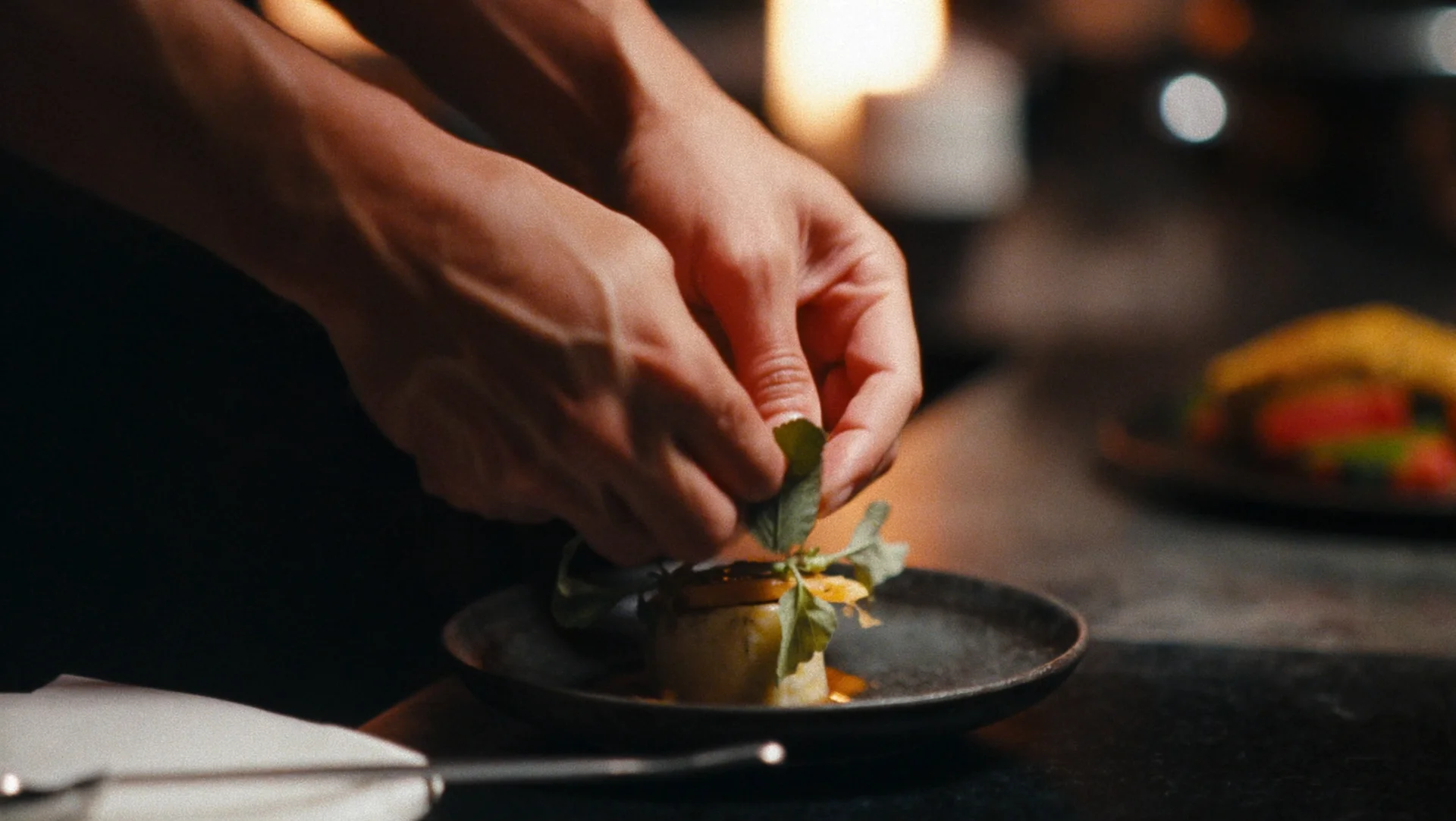 Hands finishing a plate under warm kitchen light